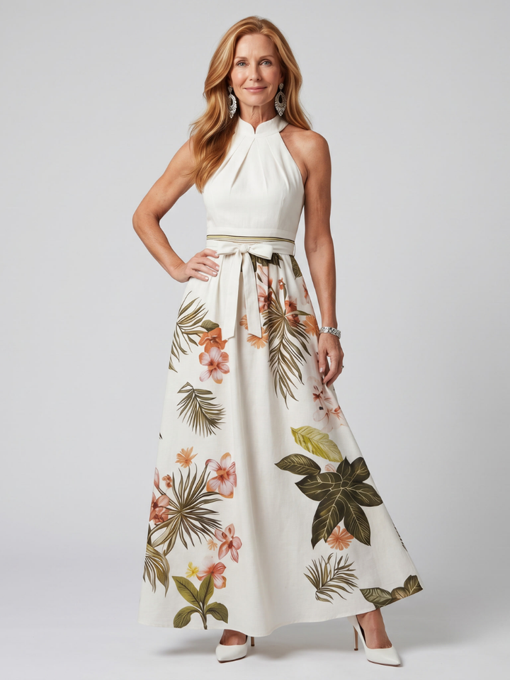 Veda Bremen Meadow maxikleid with neckholder, draped fabric, and botanical accents, shown hanging on a clothing rack.