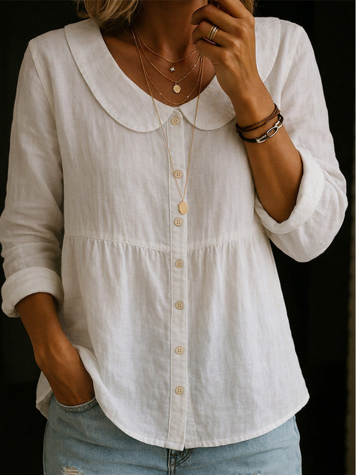 Veda Bremen Arlira linen blouse with Peter-Pan collar, soft textured fabric, displayed hanging on a wooden hanger.
